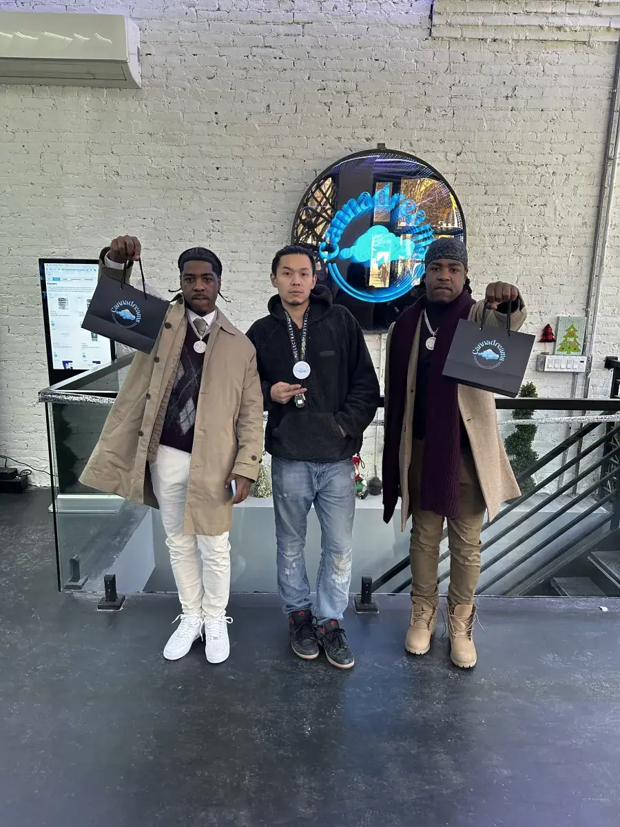 Customers holding Cannadreams bags in front of the neon Cannadreams sign