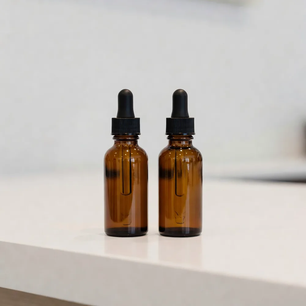 Two identical unlabeled amber glass tincture dropper bottles side by side on a white surface
